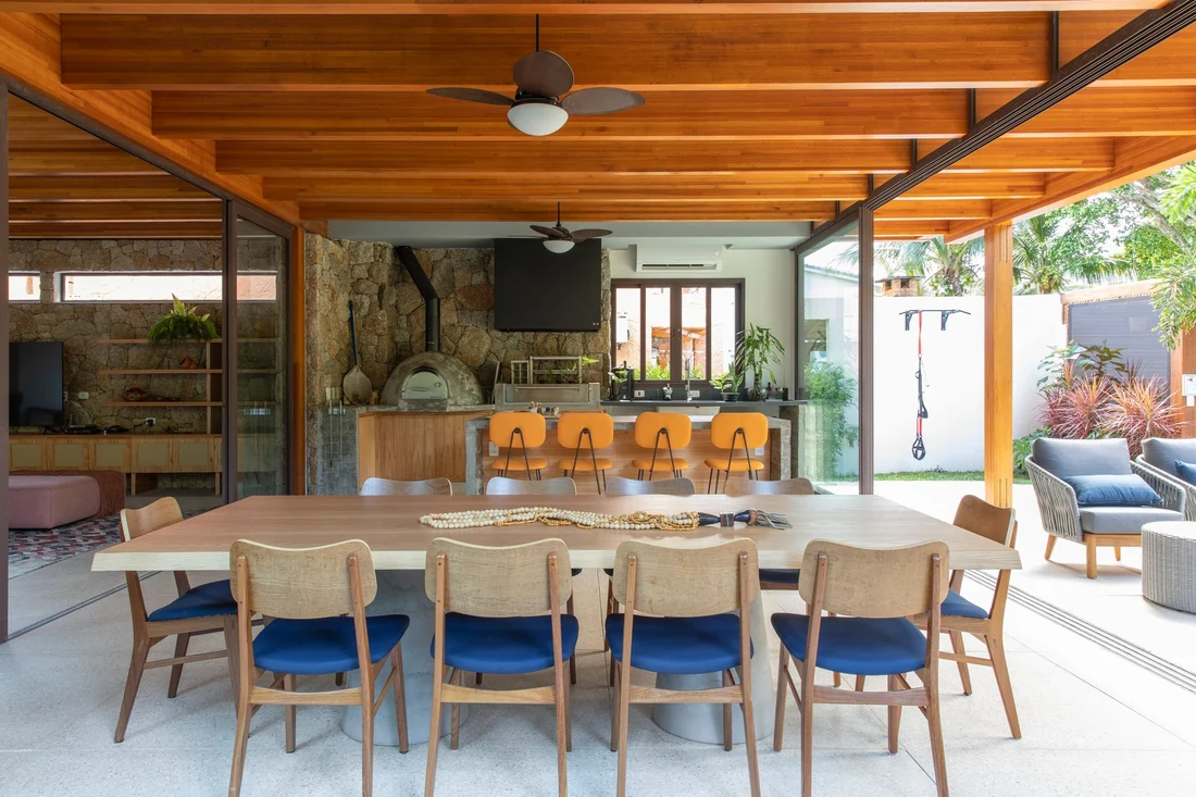 Varanda gourmet com mesa, churrasqueira e ilha, aberta para a área da piscina